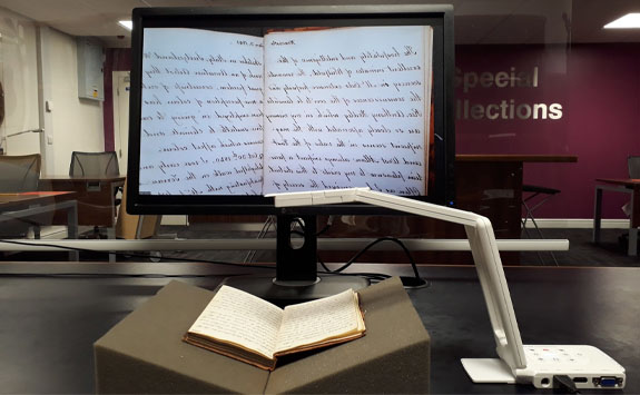 Image of a PC with an book on a book rest and a visualiser, projecting the image onto the PC